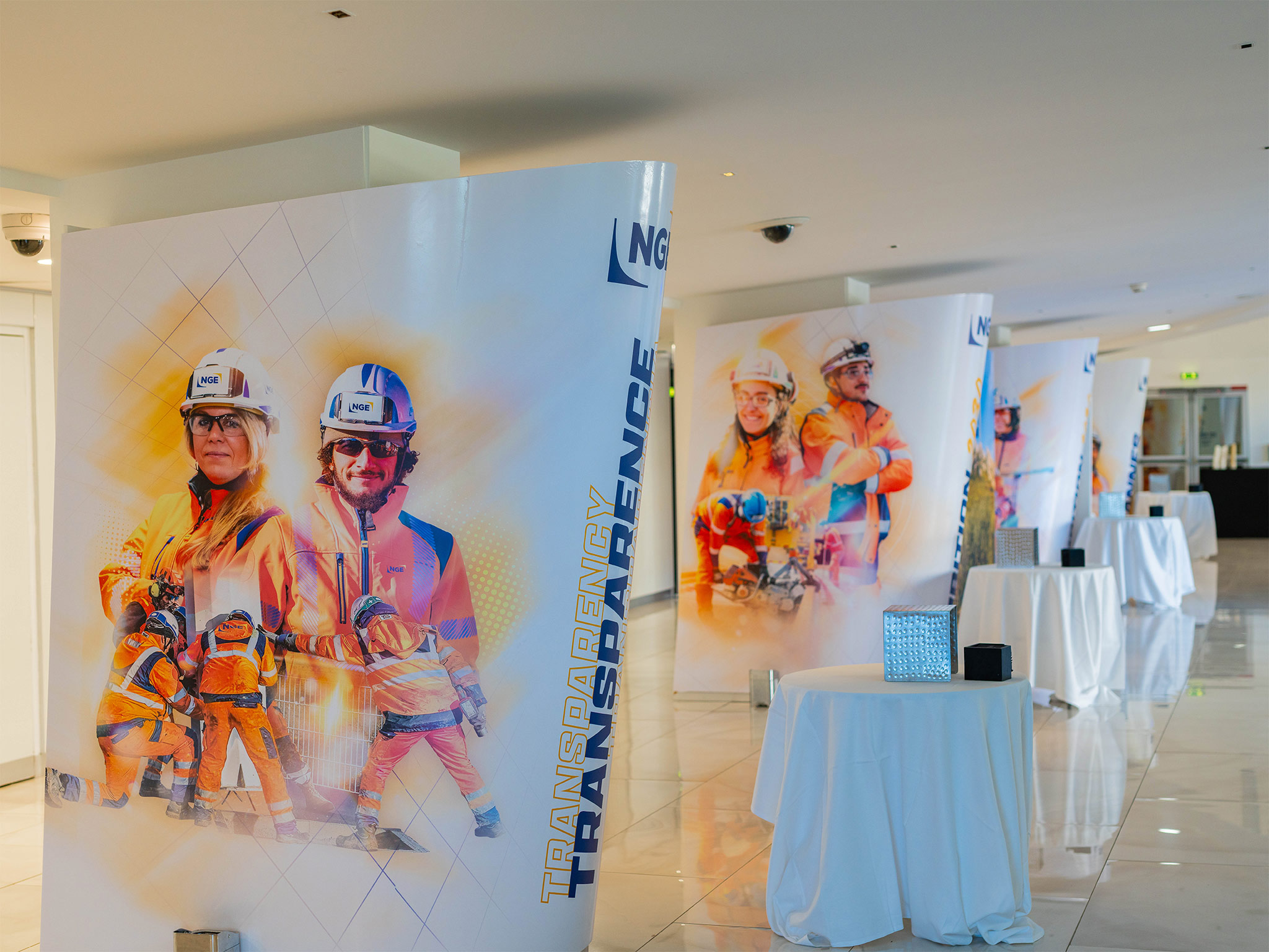 Colonnes scénographiques conçues et installées par AUCOP dans le foyer du Palais des Festivals de Cannes : habillage NGE avec portraits de collaborateurs en tenue de chantier, mise en lumière dorée sur-mesure.