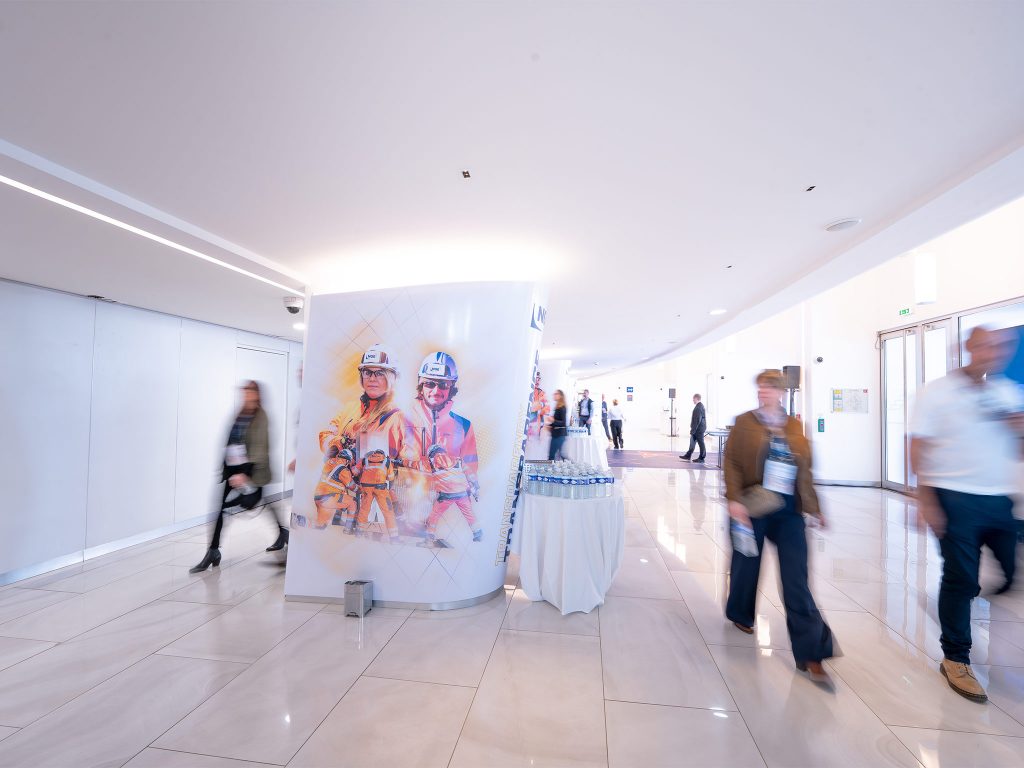 Colonnes scénographiques conçues et installées par AUCOP dans le foyer du Palais des Festivals de Cannes : habillage NGE avec portraits de collaborateurs en tenue de chantier, mise en lumière dorée sur-mesure.