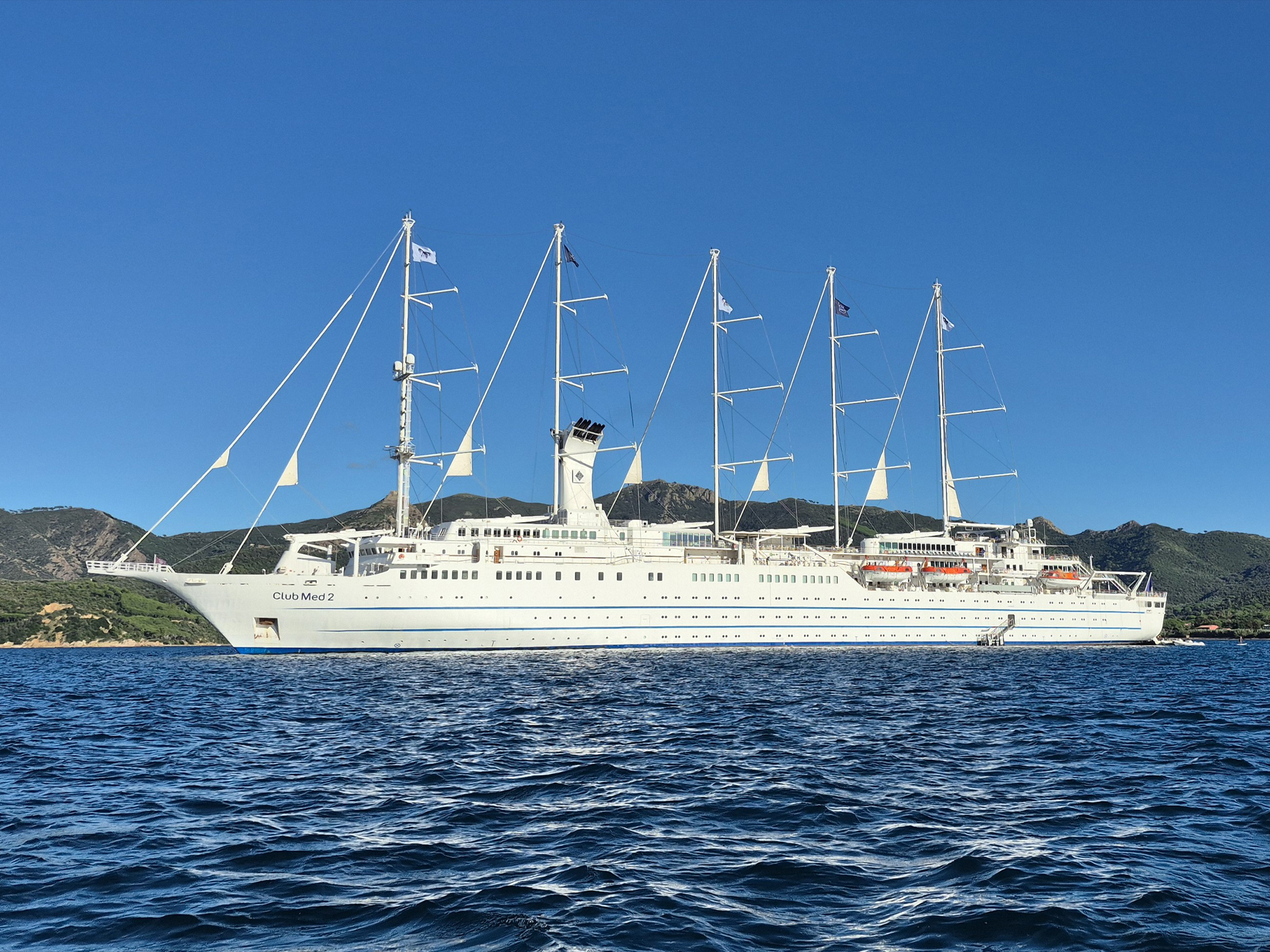 Le Club Med 2, voilier à cinq mâts, naviguant en Méditerranée sous un ciel bleu avec les collines en arrière-plan — cadre de la convention corporate produite par AUCOP Event, Côte d'Azur