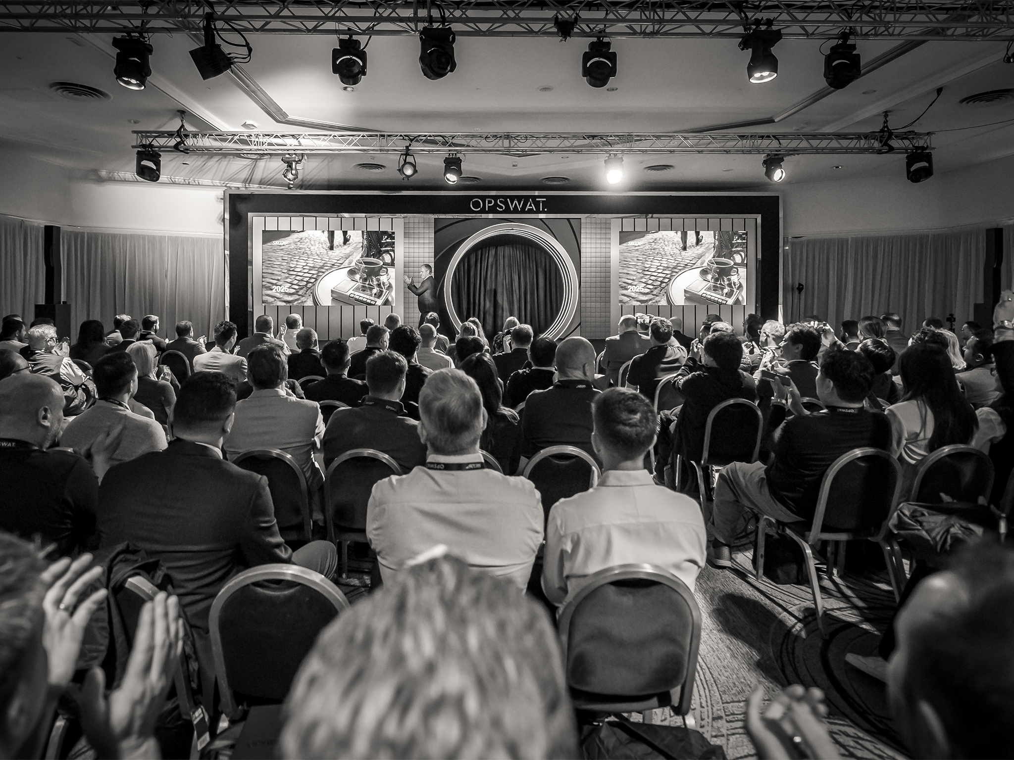 Plénière du SKO26 d'OPSWAT en noir et blanc : salle comble face à la scène conçue par AUCOP, avec son arche à LED incrustées et son backdrop sur mesure, murs LED ROE Diamond 2.6 mm pilotés par AUCOP et captation par caméras robotisées 4K.