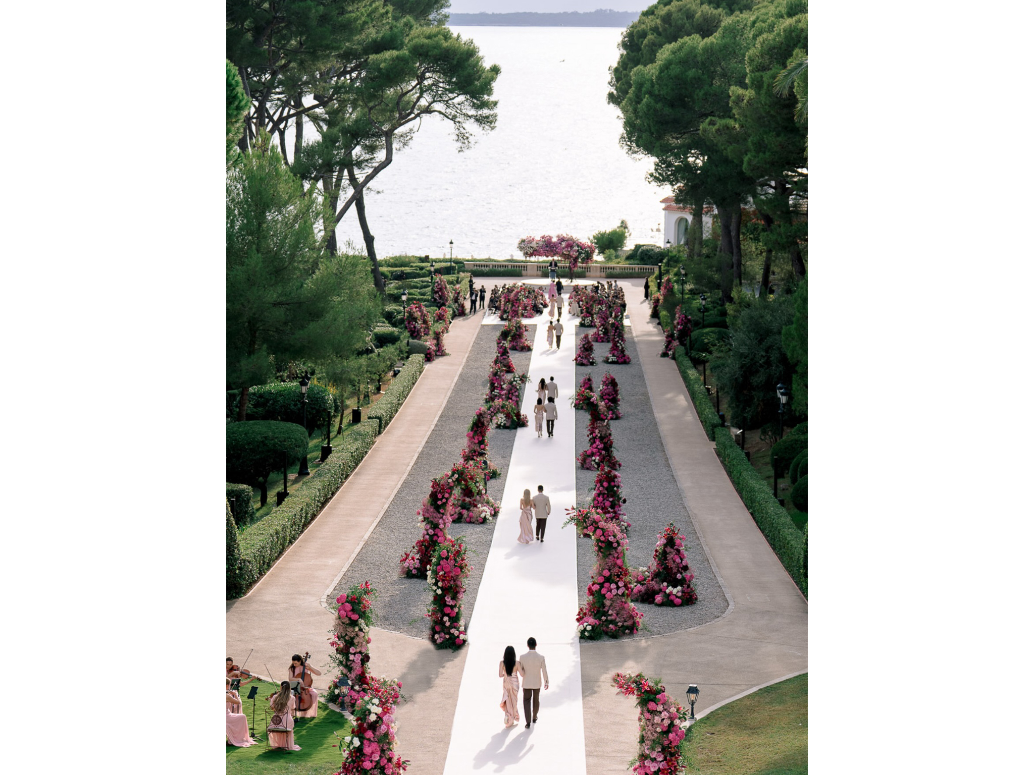 Allée de cérémonie vue du ciel avec colonnes de fleurs roses et tapis blanc au mariage d'Angelina & Kelvin à l'Hôtel du Cap-Eden-Roc — production AUCOP
