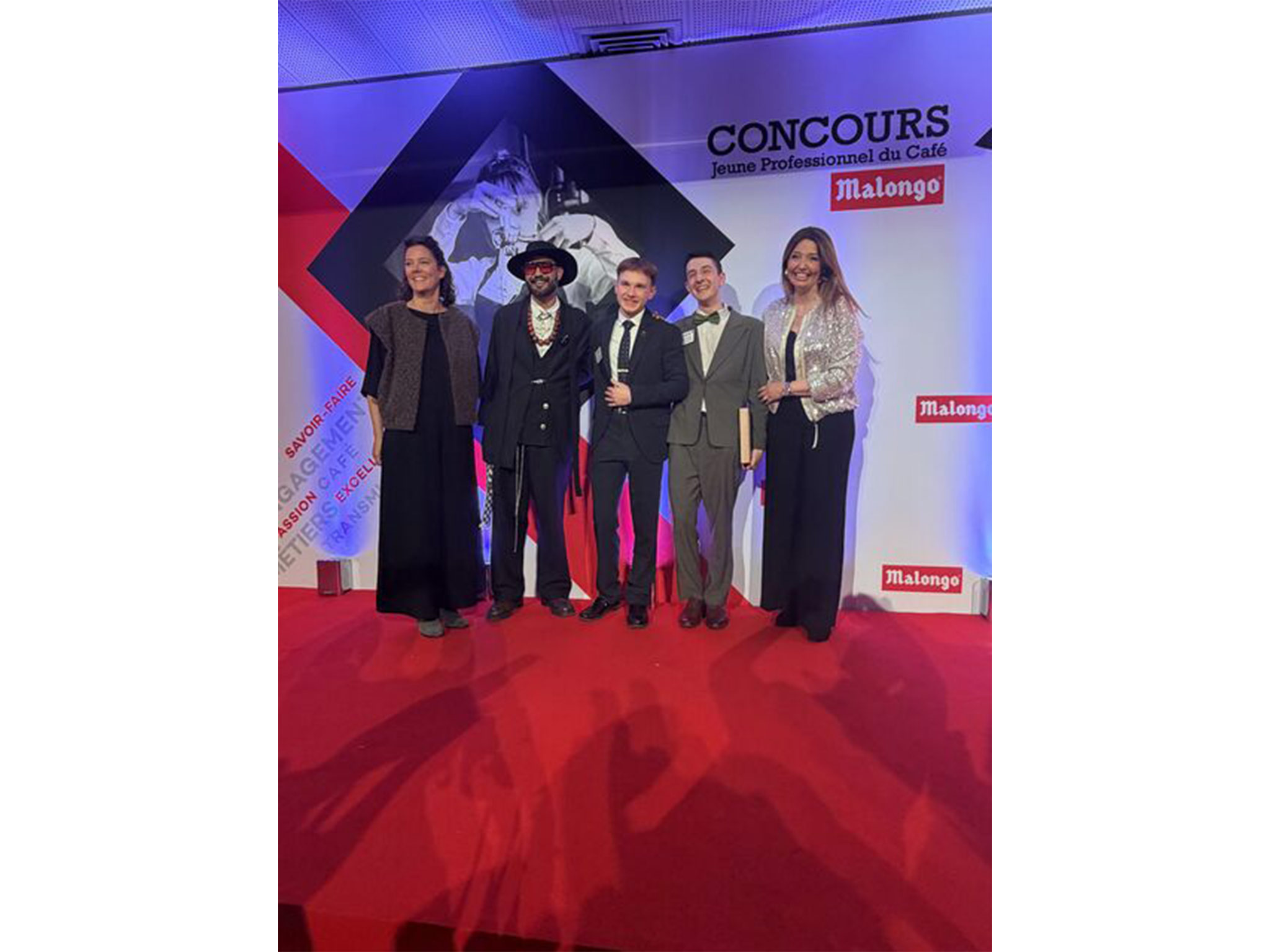 Photo de groupe sur scène lors de la remise des prix du Concours Malongo 2026 à Nice — lauréats et membres du jury devant le fond photocall Malongo réalisé par AUCOP.