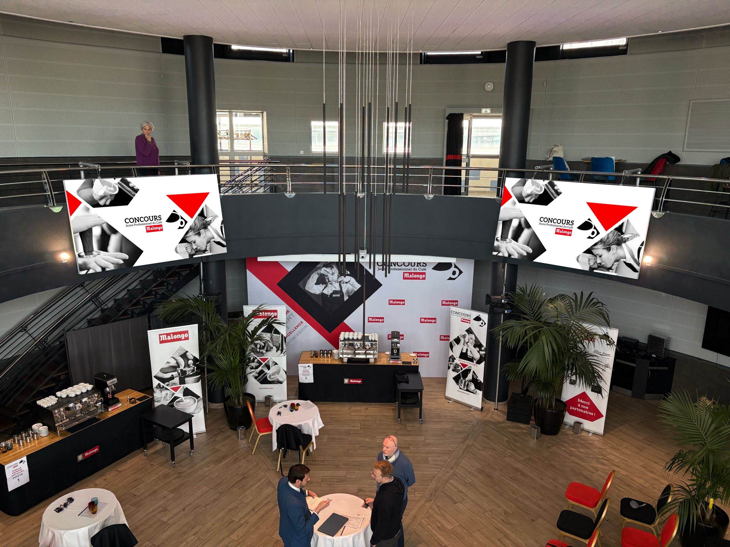 Vue d'ensemble de la salle lors de la journée de compétition du Concours Malongo 2026 à Nice : écrans LED, fond de scène Blacktex et tables de dégustation café