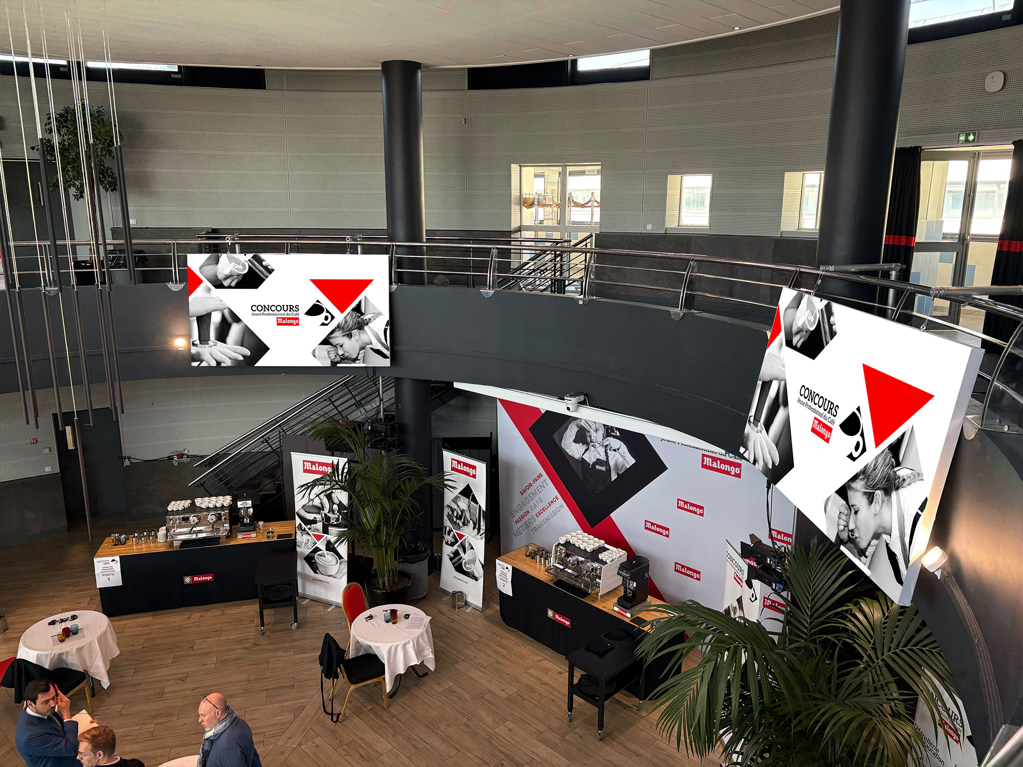 Double écrans LED affichant le visuel du Concours Malongo lors de la journée de compétition à Nice, vus depuis la mezzanine — installation AUCOP, avril 2026.