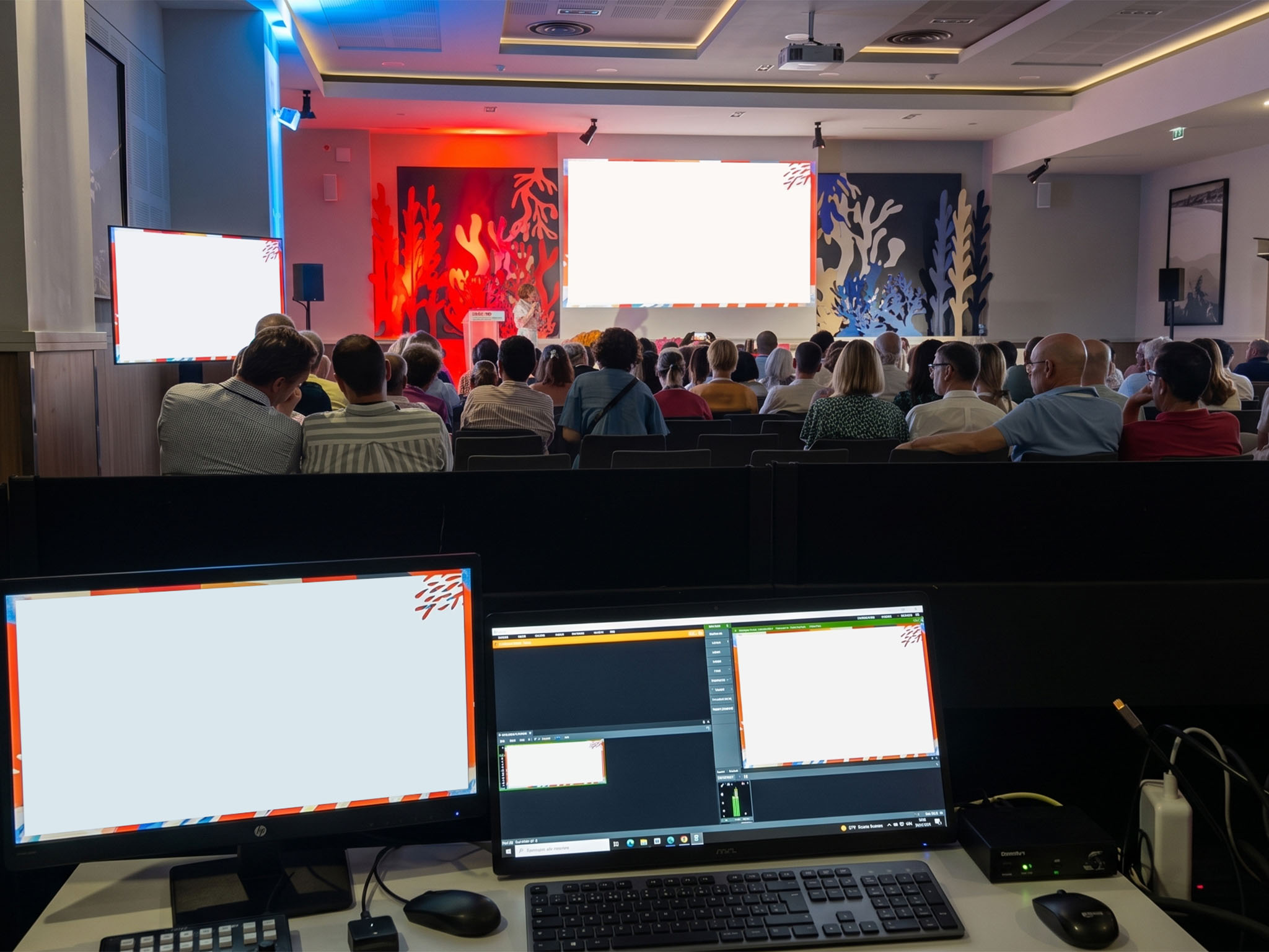 Régie audiovisuelle AUCOP au premier plan pendant une convention au Radisson Blu de Nice, public et intervenante sur scène en arrière-plan.