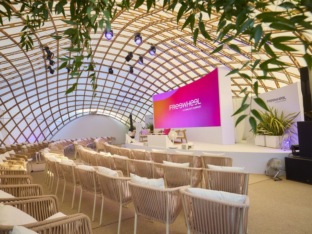 aucop-creative spirit-mur-led-eclairage-scene-voute-bois-plage-freewheel-cannes-lions-2026 Scène de la plage FreeWheel avant ouverture, Cannes Lions 2026 : mur LED aux couleurs FreeWheel et projecteurs asservis en création lumière — installation vidéo et lumière Aucop, sous la voûte en bois.