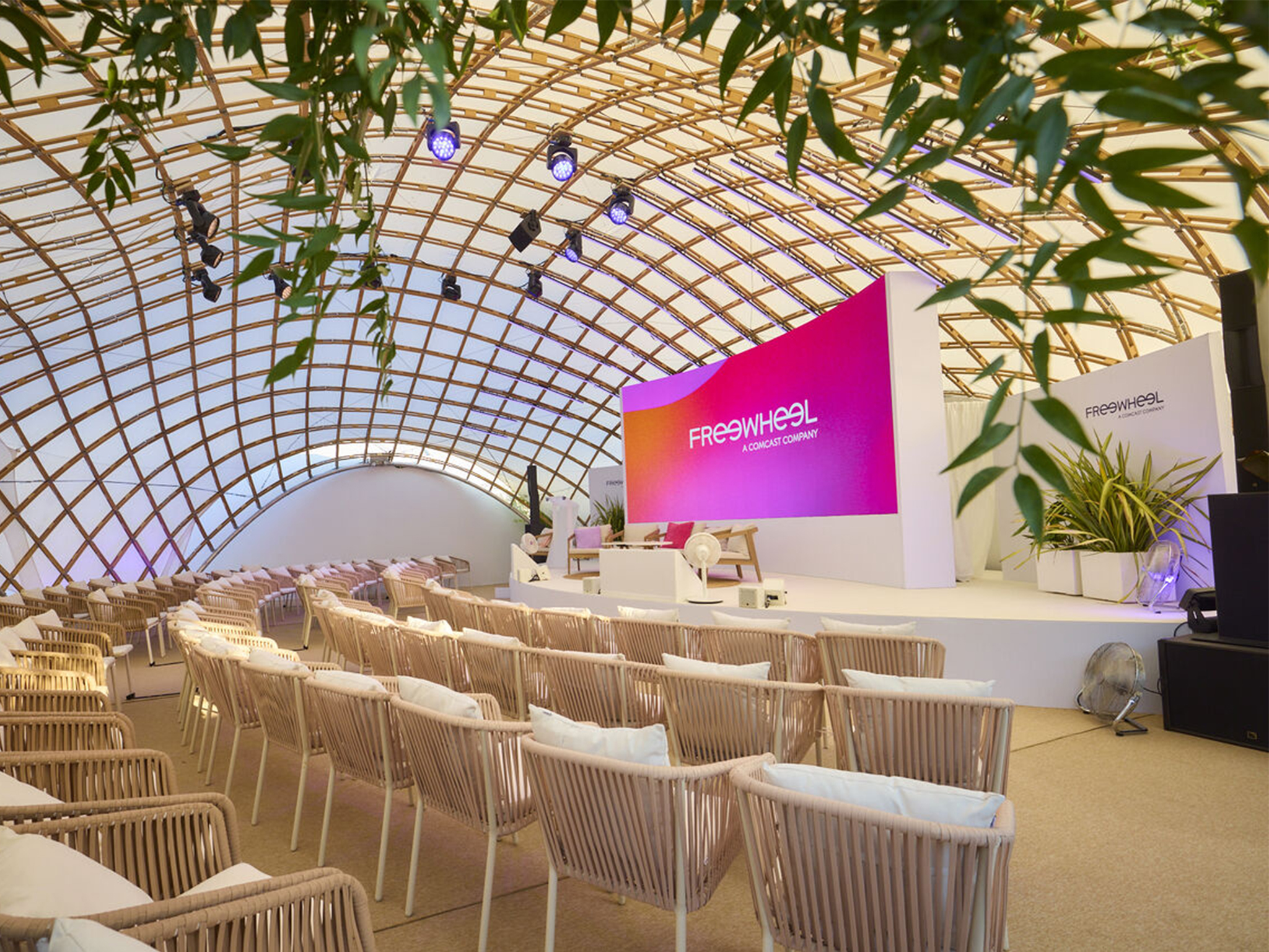 Scène de la plage FreeWheel avant ouverture, Cannes Lions 2026 : mur LED aux couleurs FreeWheel et projecteurs asservis en création lumière — installation vidéo et lumière Aucop, sous la voûte en bois.