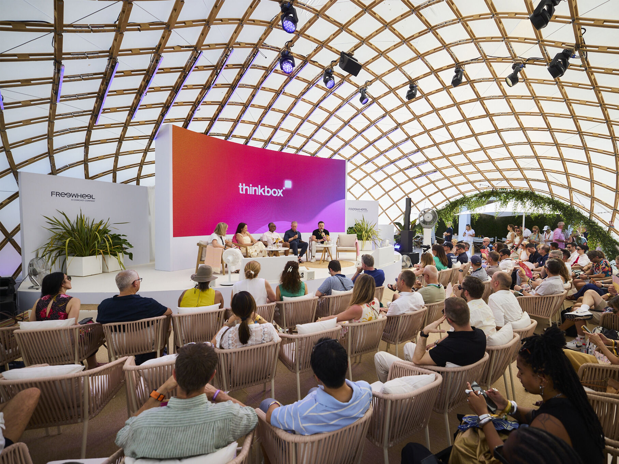 Conférence sous la voûte en bois de la plage FreeWheel aux Cannes Lions 2026 : mur LED courbe haute définition, projecteurs asservis et sonorisation déployés par Aucop, salle comble face à la scène.