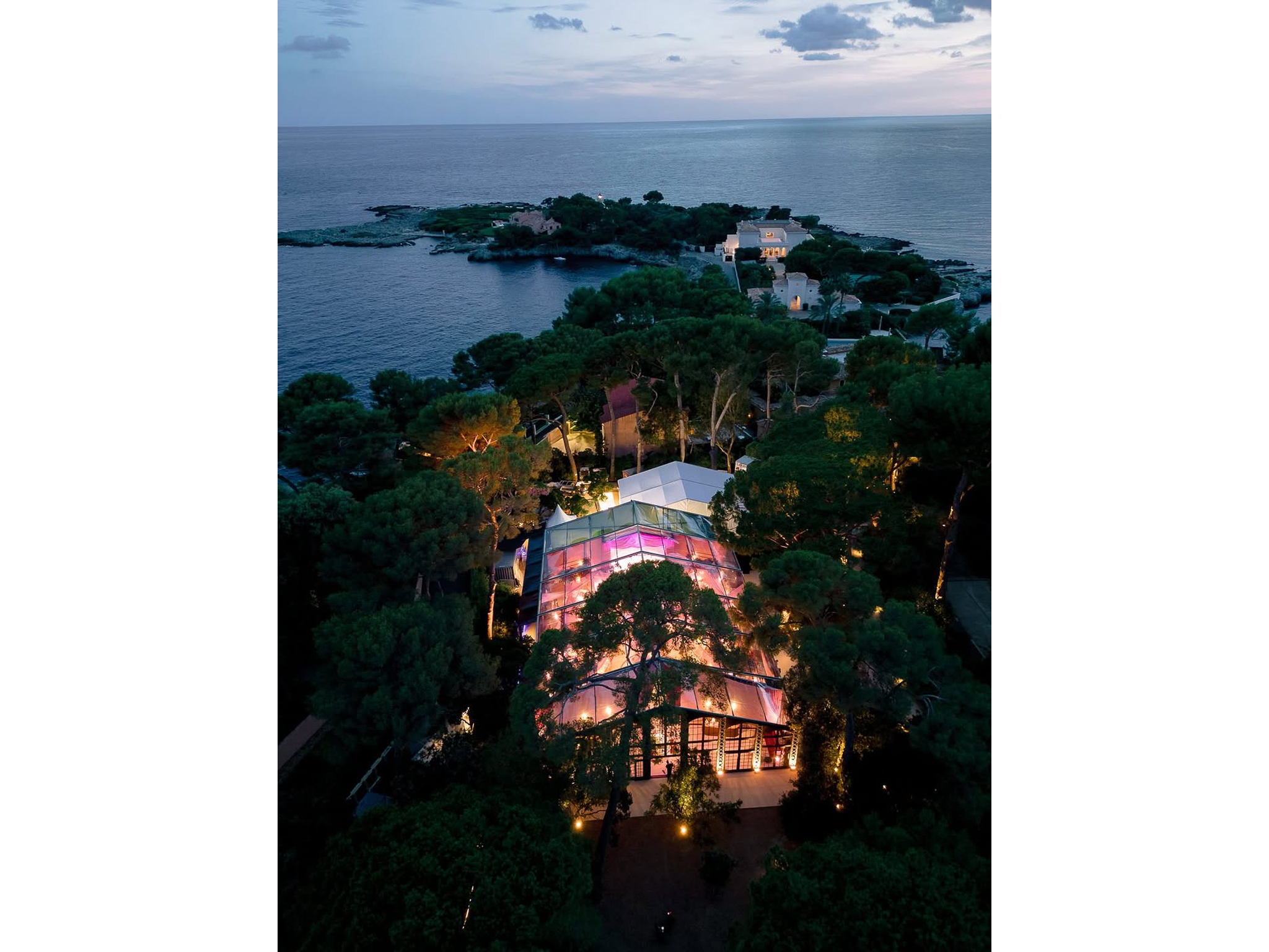 Vue nocturne de la salle de soirée du mariage à l'Hôtel du Cap-Eden-Roc : plafond floral rose et bordeaux, bougies pendantes, bar arrondi AUCOP, invités attablés