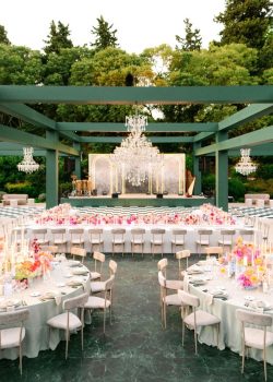 AUCOP - Espace dîner sous la pergola en bois peint vert : lustres en cristal suspendus, scène avec fond marbré, harpe et batterie, piste de danse damier et tables fleuries aux tons pastel - scénographie White Eden Weddings, production AUCOP, Airelles Château d'Estoublon, Provence