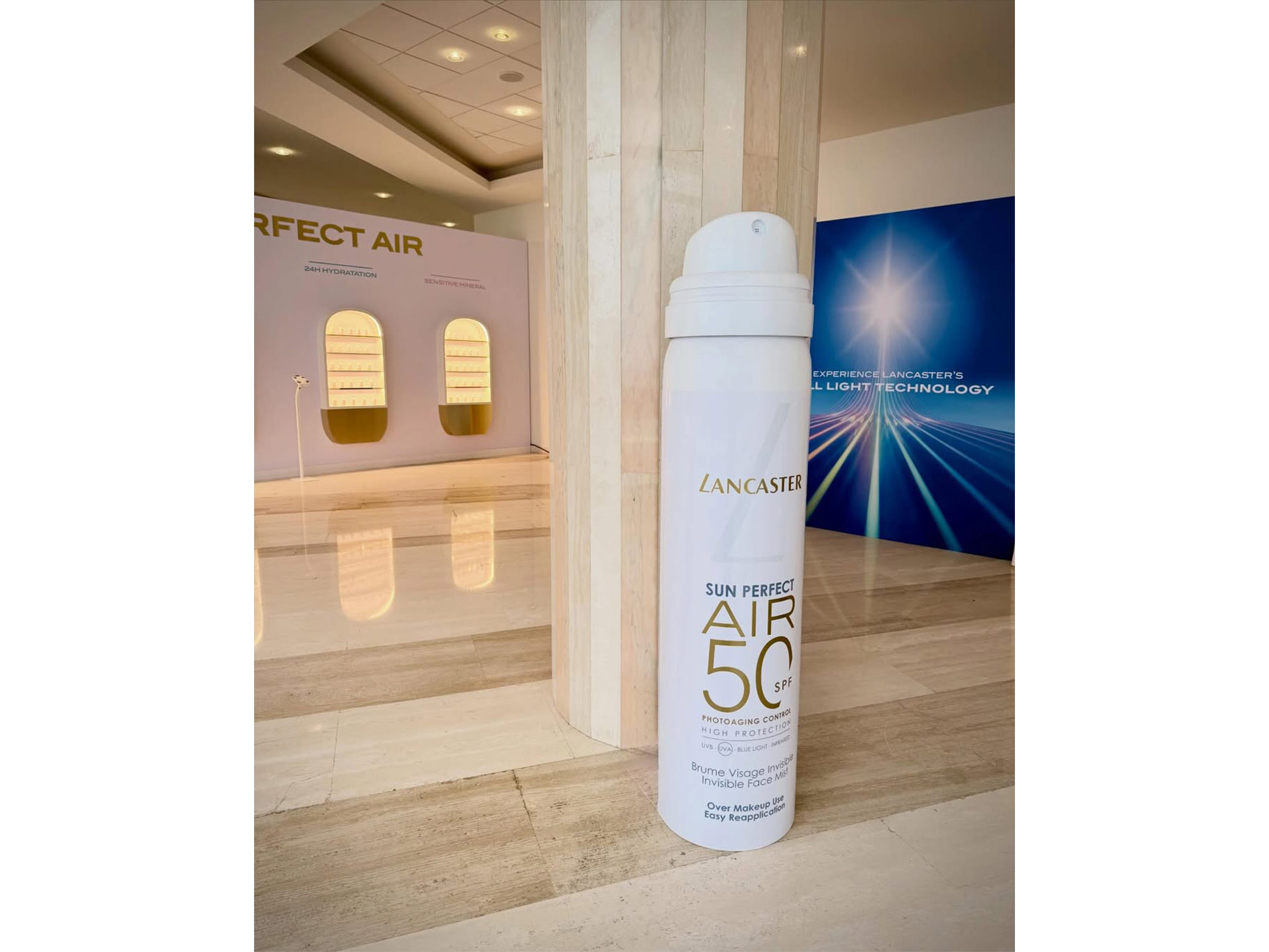 Produit Sun Perfect Air SPF 50 Lancaster Monaco au premier plan – showroom rétroéclairé sur mesure AUCOP en arrière-plan, UV Science Summit 2026