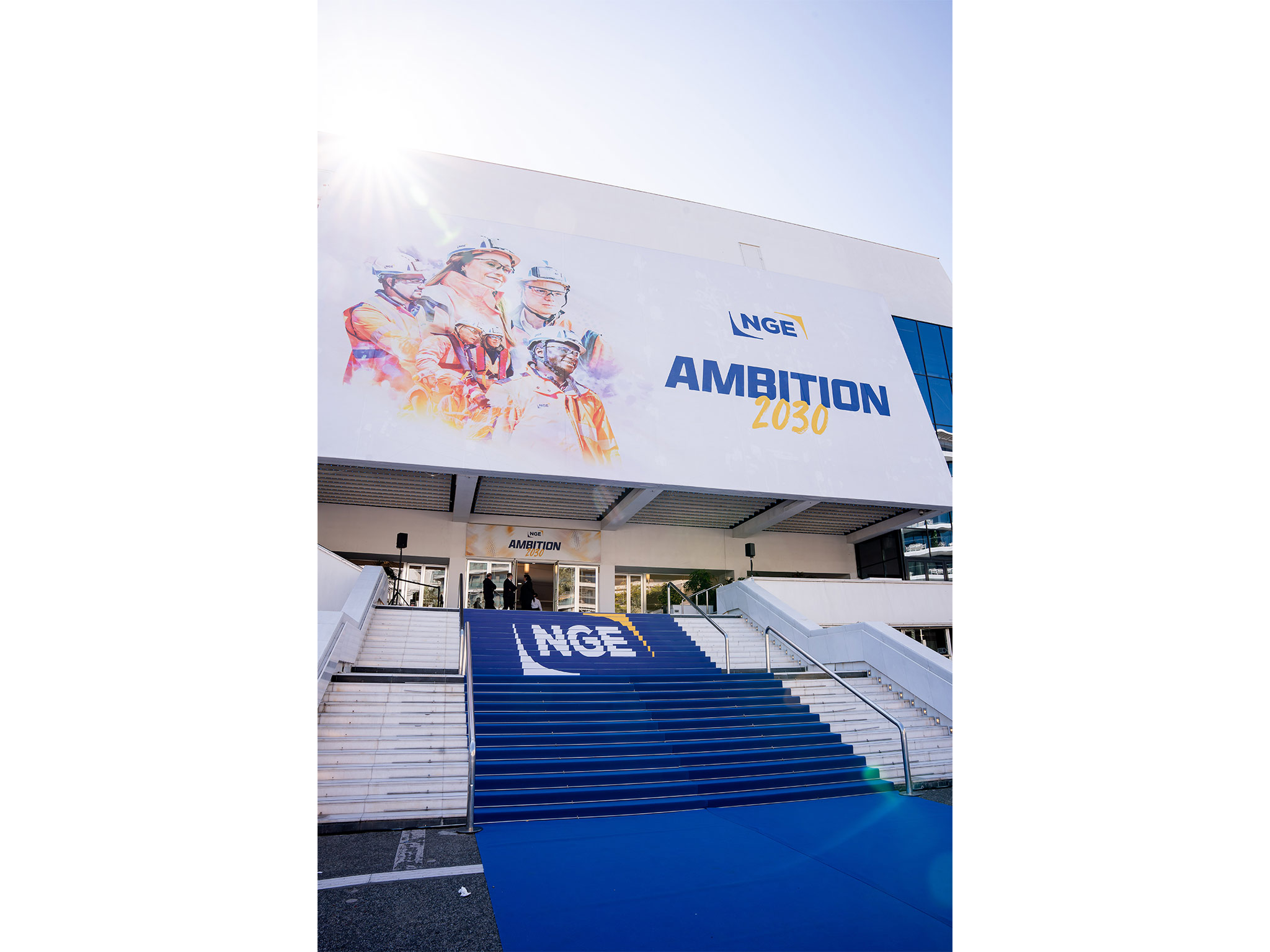 Façade du Palais des Festivals de Cannes habillée par AUCOP pour la convention NGE Ambition 2030 : grande bâche illustrée, marches et tapis bleu NGE, sky tracers et sonorisation extérieure.