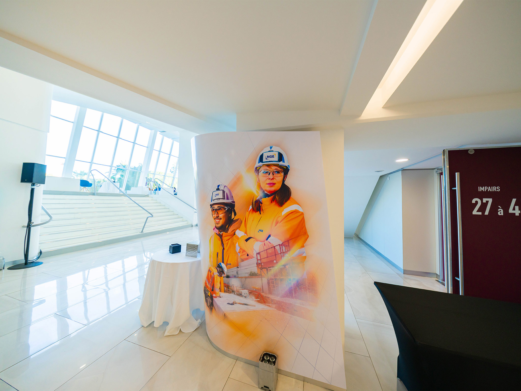 Colonnes scénographiques conçues et installées par AUCOP dans le foyer du Palais des Festivals de Cannes : habillage NGE avec portraits de collaborateurs en tenue de chantier, mise en lumière dorée sur-mesure.