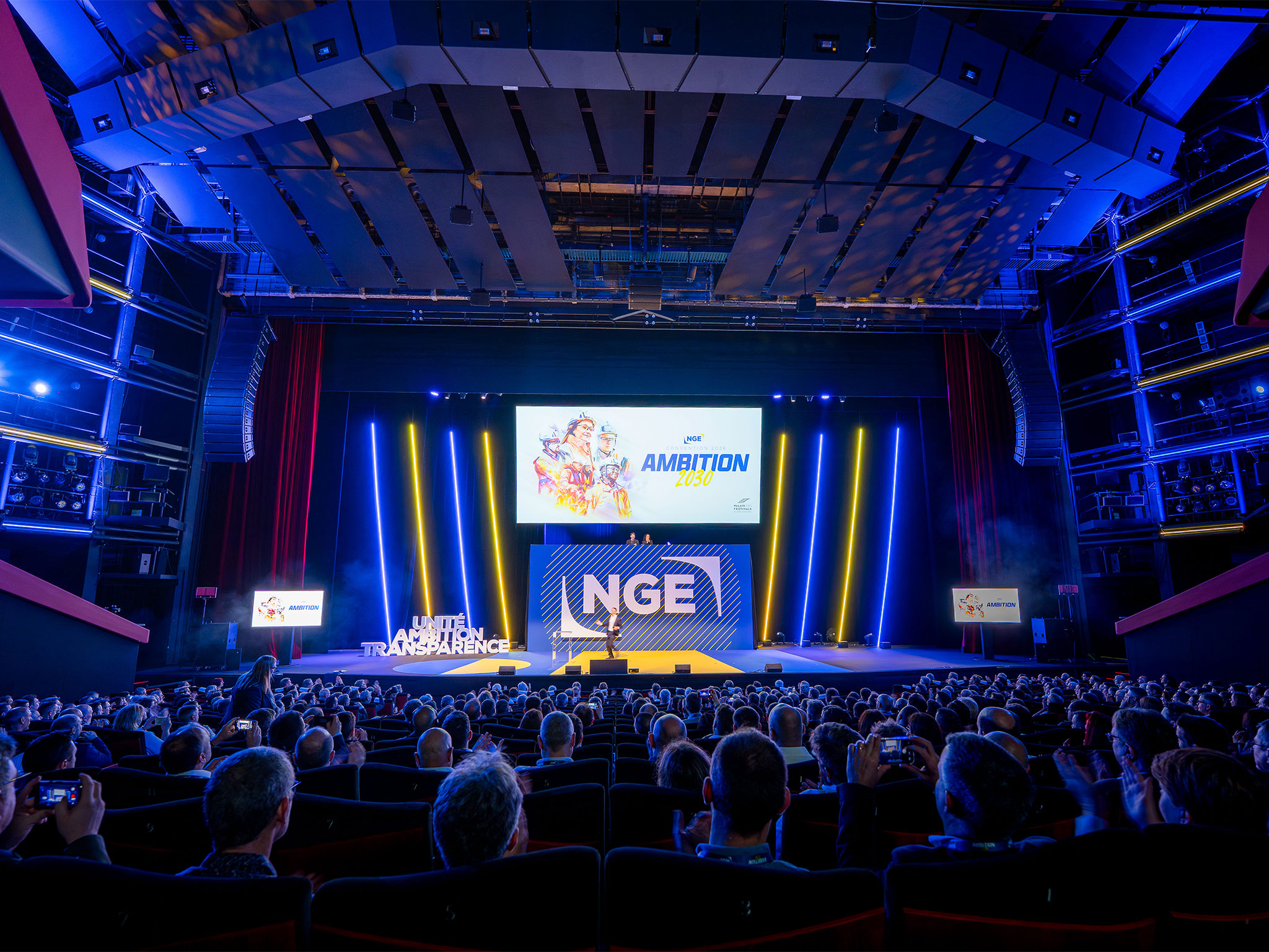 Auditorium du Palais des Festivals comble lors de la plénière NGE Ambition 2030 : fond de scène, logo NGE illuminé, vidéoprojection et mise en lumière signés AUCOP, plus de 1 000 collaborateurs en salle.