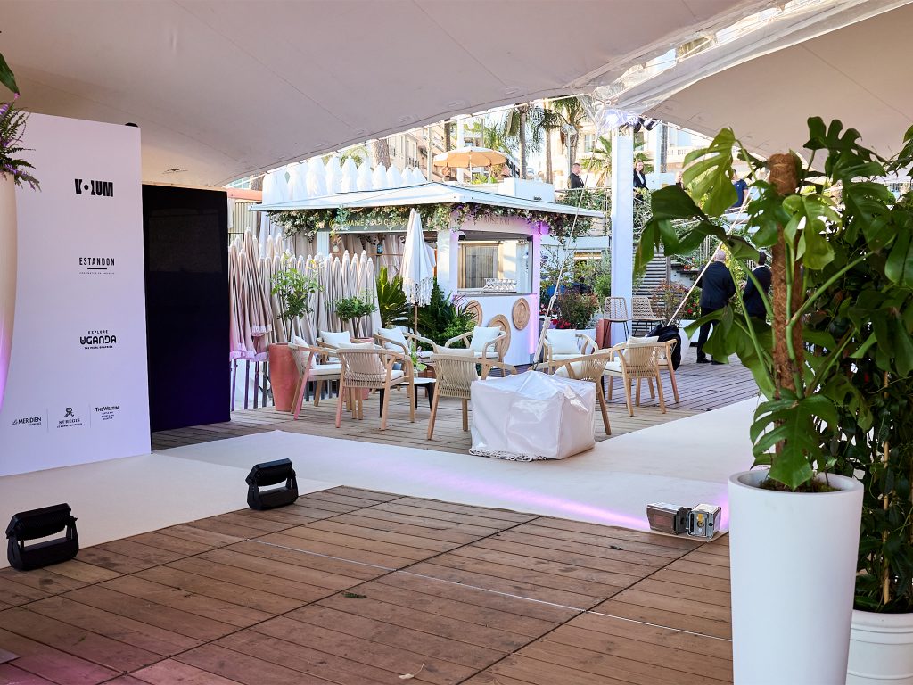 Photocall step-and-repeat sponsors de la soirée Akili Mirari au FIF Cannes 2026 : backdrop blanc avec logos Allociné, K-Lum, Explore Uganda, Estandon, Le Méridien, installé et éclairé par les équipes AUCOP