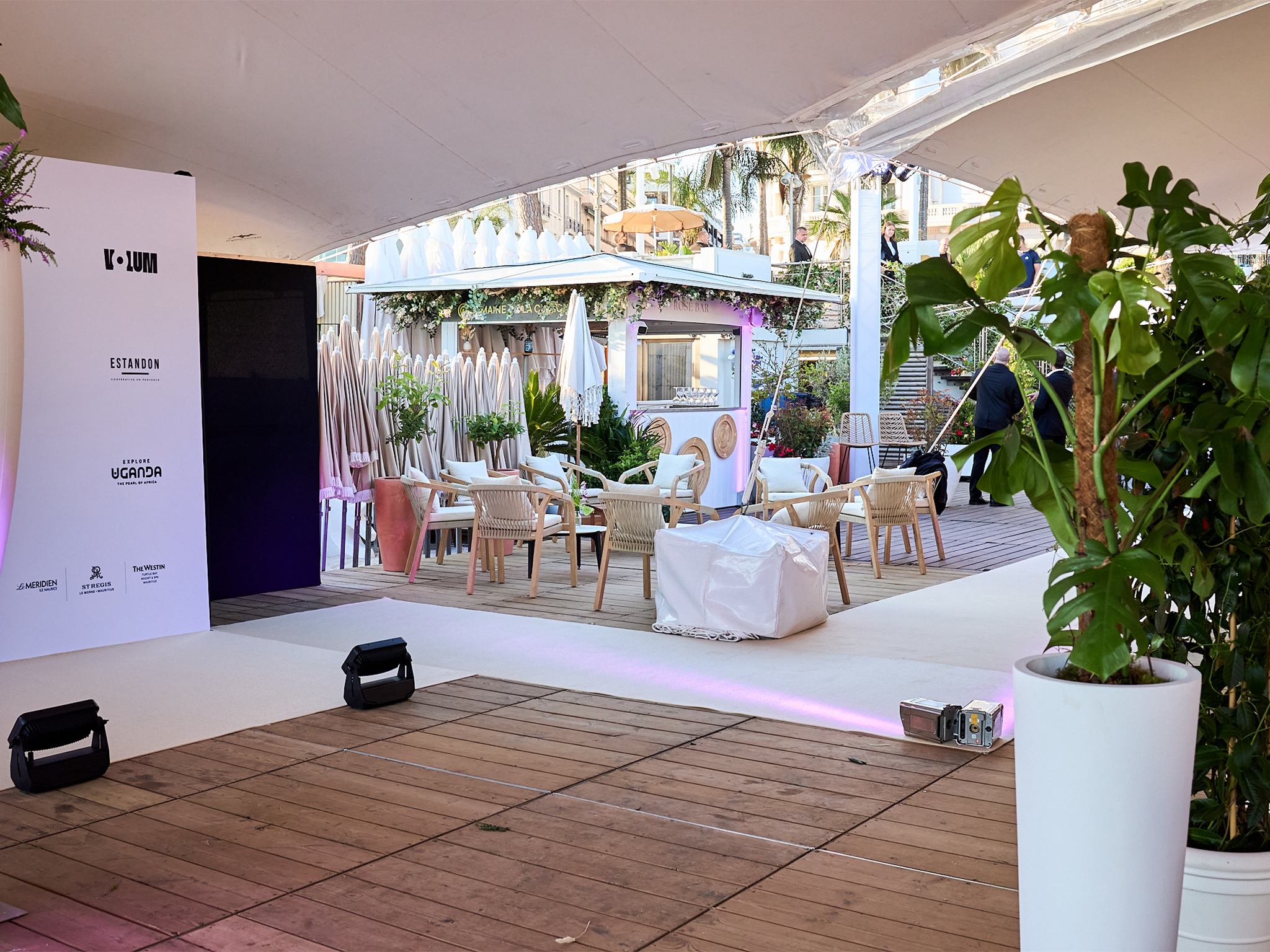 Photocall step-and-repeat sponsors de la soirée Akili Mirari au FIF Cannes 2026 : backdrop blanc avec logos Allociné, K-Lum, Explore Uganda, Estandon, Le Méridien, installé et éclairé par les équipes AUCOP