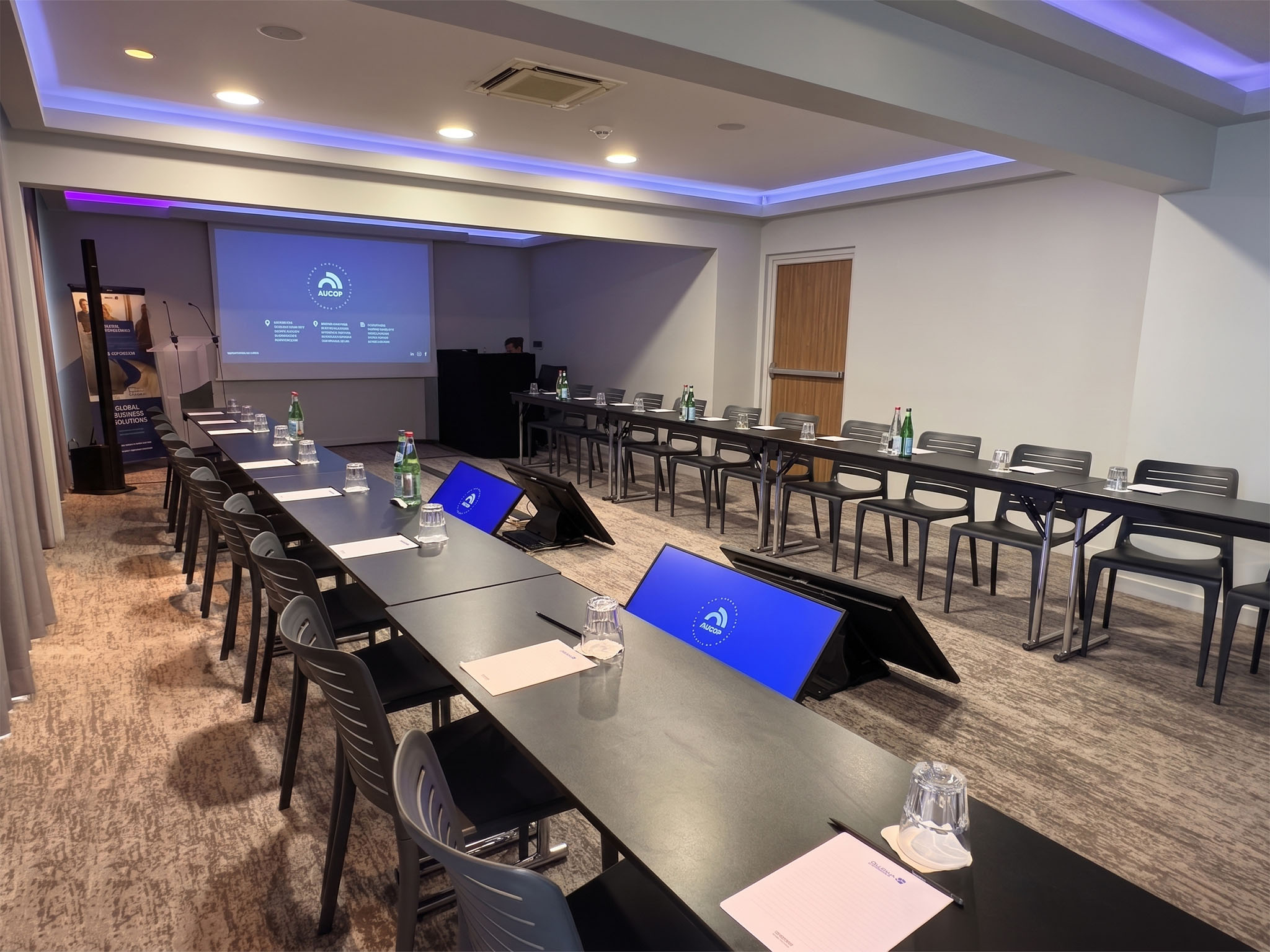 Écrans de retour affichant le logo AUCOP dans le U d'un séminaire au Radisson Blu de Nice, avec vidéoprojection et régie en arrière-plan.