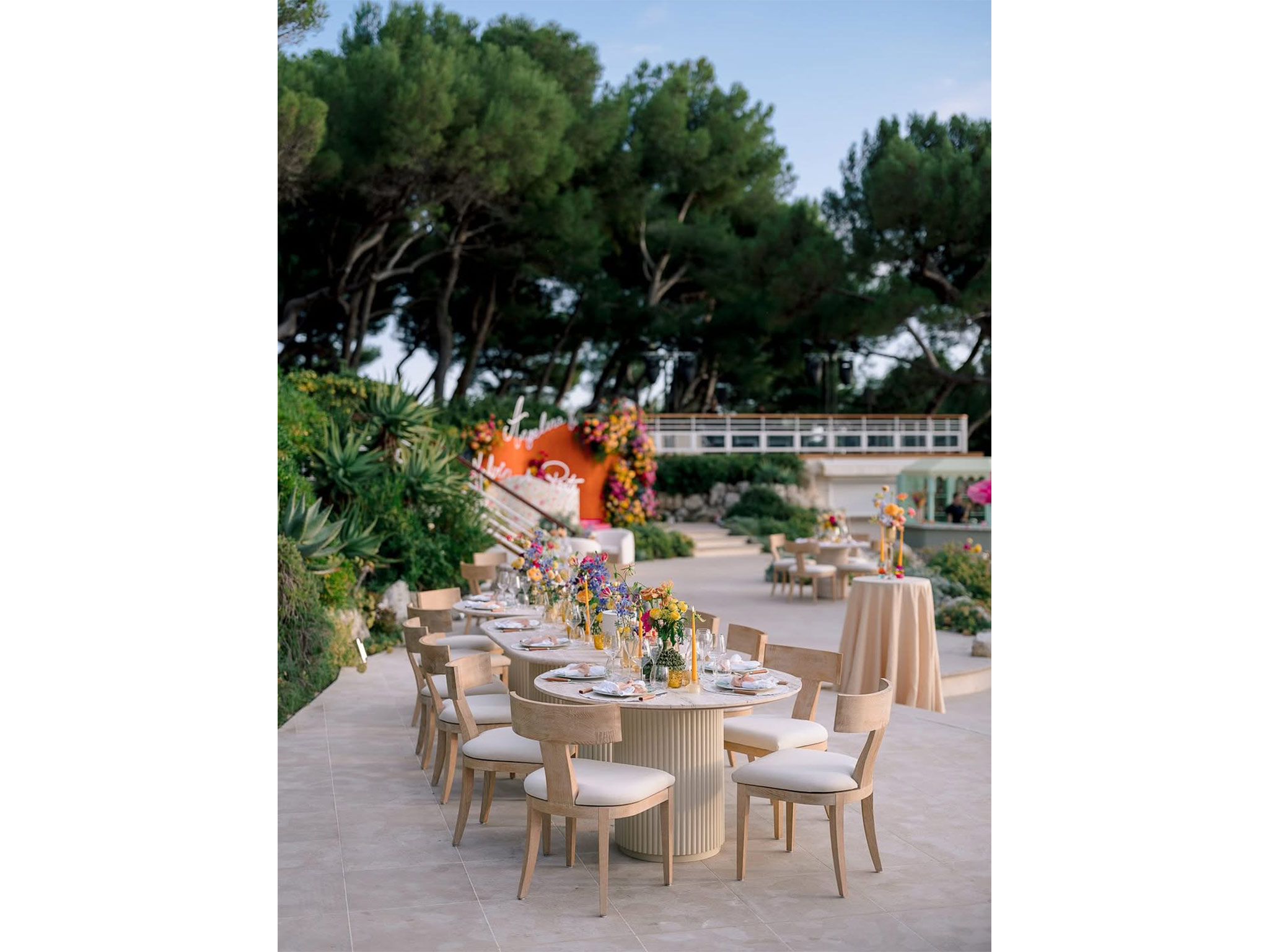 Vue générale de la terrasse du Welcome Dinner d'Angelina & Kelvin à l'Hôtel du Cap Eden Roc — tables dressées, bar arrondi sous dôme orange, bar à spritz vert menthe, fleurs géantes et vue panoramique sur la Méditerranée, production AUCOP et White Eden Weddings.