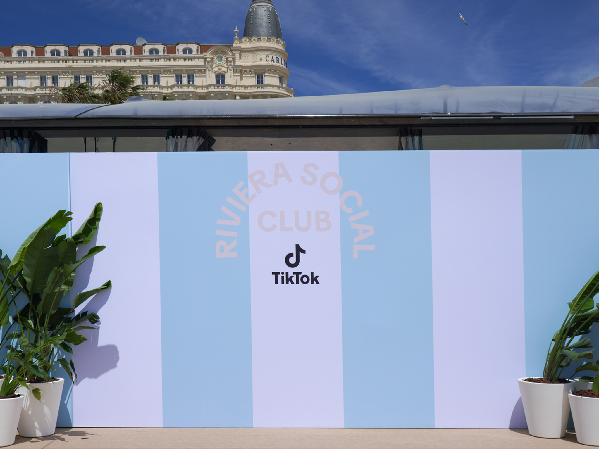 Grand mur de photocall extérieur à larges rayures bleues et blanches avec l’inscription "Riviera Social Club TikTok", installé sur la Croisette à Cannes par AUCOP avec l'hôtel Carlton visible en arrière-plan