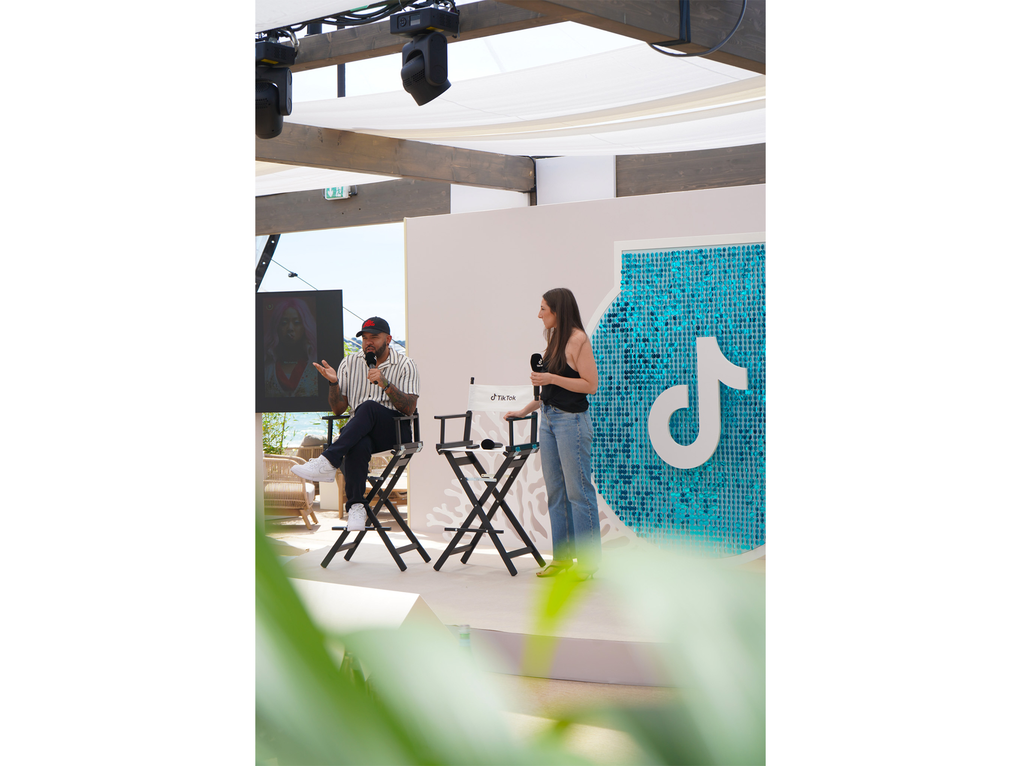 Prise de parole et workshop sur la scène TikTok de la Plage Vegaluna à Cannes : intervenants assis sur des chaises de réalisateur équipés de micros, devant le décor scénographique en sequins turquoise et coraux blancs fabriqué par AUCOP.