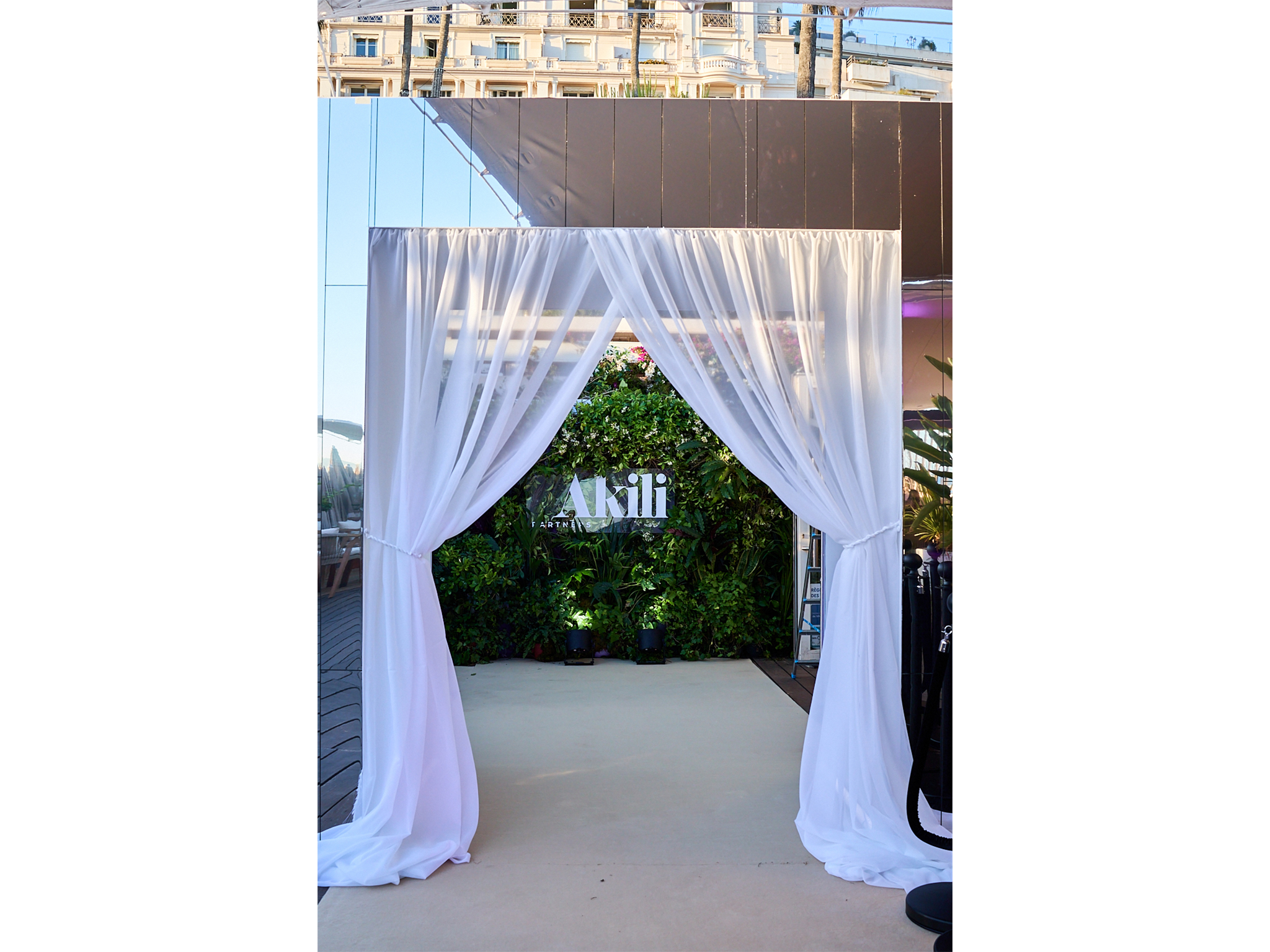 Tunnel immersif sur mesure réalisé par AUCOP pour la soirée Akili Mirari au Festival de Cannes 2026 : voilages blancs drapés et panneaux miroirs sur la plage Croisette Beach