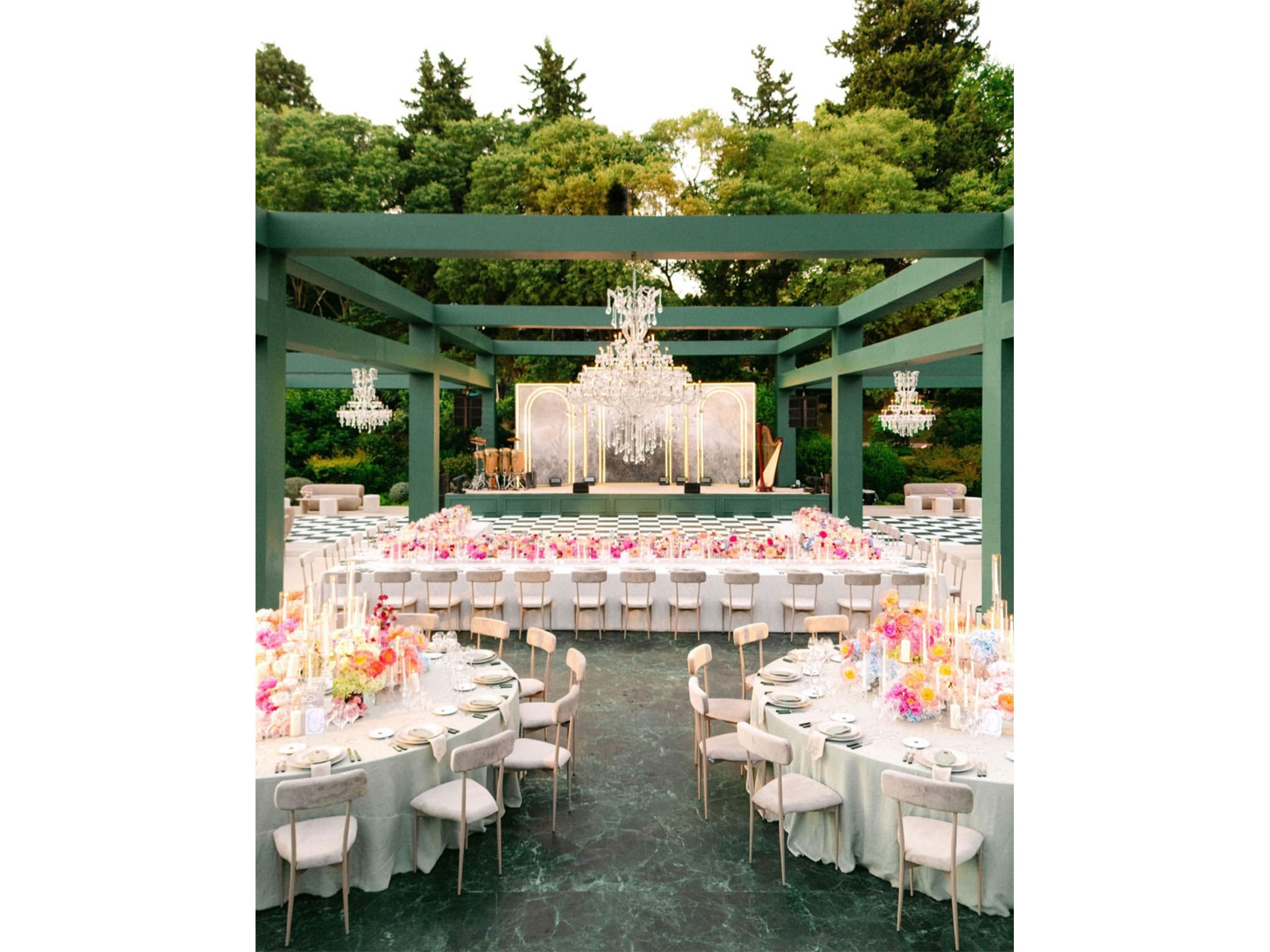 AUCOP - Espace dîner sous la pergola en bois peint vert : lustres en cristal suspendus, scène avec fond marbré, harpe et batterie, piste de danse damier et tables fleuries aux tons pastel - scénographie White Eden Weddings, production AUCOP, Airelles Château d'Estoublon, Provence