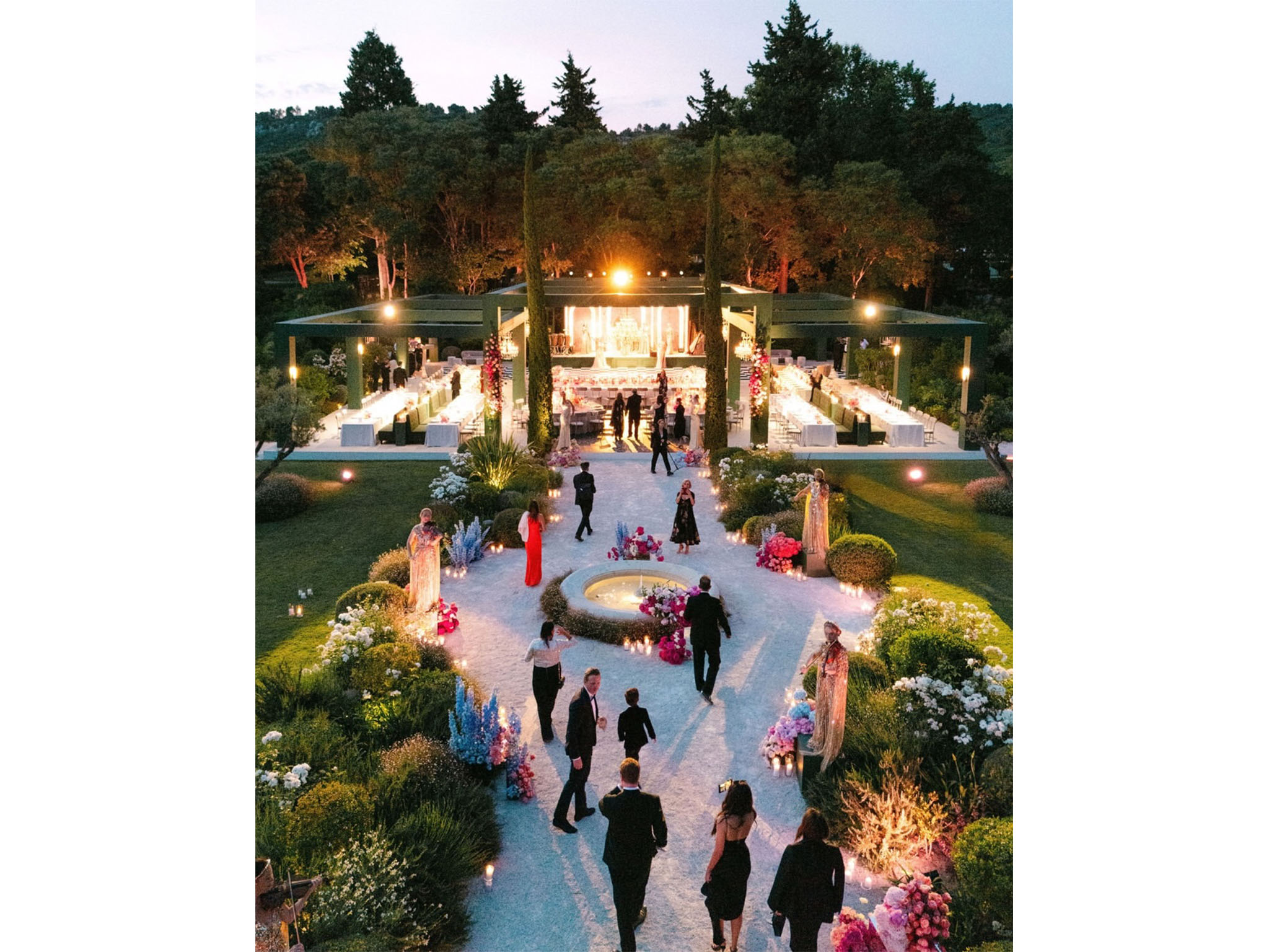 AUCOP - Dîner de mariage au crépuscule sous la pergola-structure en bois peint vert, allée en gravier blanc bordée de deux fontaines et de massifs floraux, invités en tenue de soirée - scénographie White Eden Weddings, production AUCOP, Airelles Château d'Estoublon, Provence