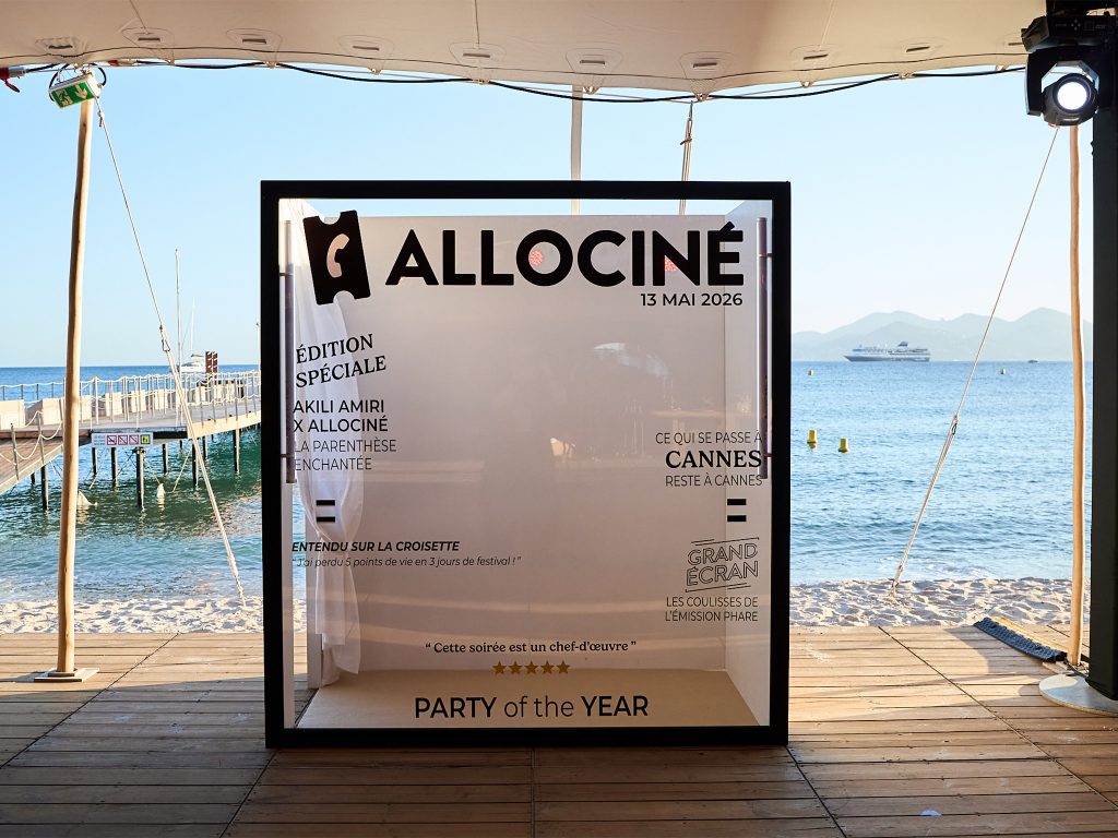 Une box photobooth en plexiglas personnalisée aux couleurs d'Allociné, partenaire média, installée côté espace expo. Soirée Akili Mirari au Festival de Cannes 2026.