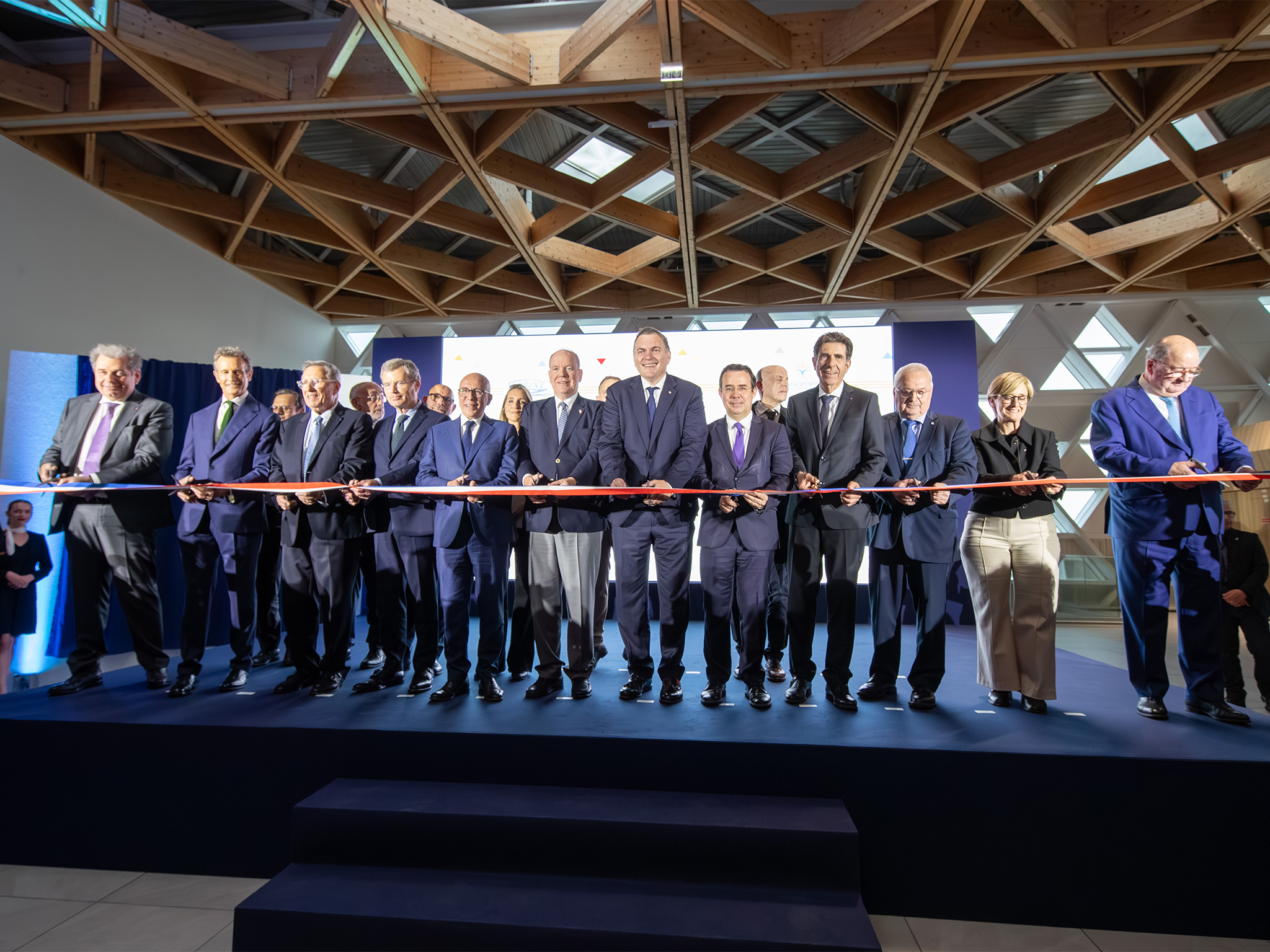 Cérémonie du ruban inaugural avec une quinzaine de personnalités alignées sur une estrade, sous la structure en bois du terminal, aucop, prestataire technique audiovisuelle et creation de decors sur mesure