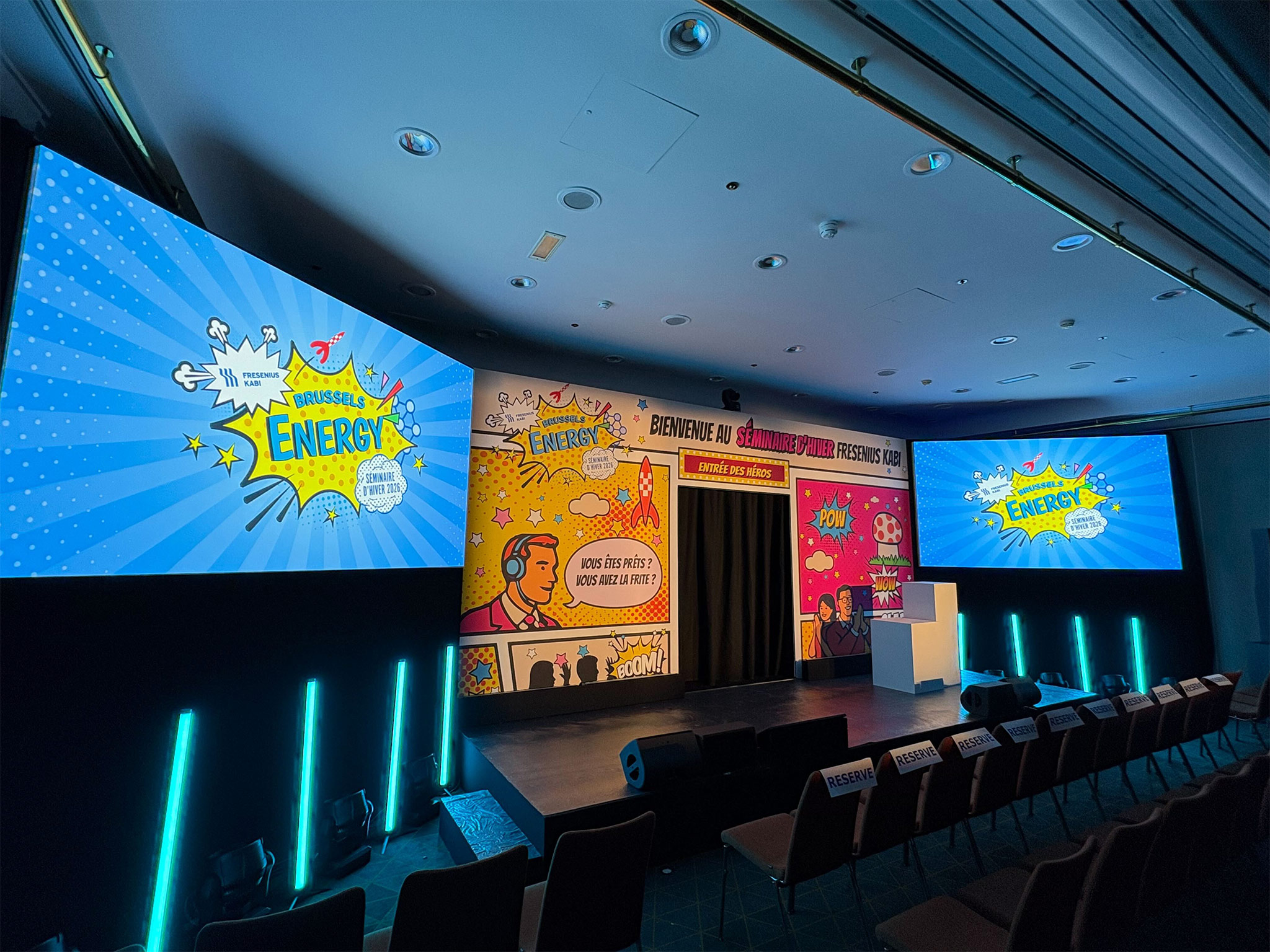 QUAND LA SCENOGRAPHIE DEVIENT UNE BANDE DESSINEE GEANTE-Scénographie pop art bande dessinée pour le séminaire corporate Brussels Energy — fond de scène impression grand format avec entrée des héros, murs latéraux sur châssis et éclairage LED, Aucop Paris