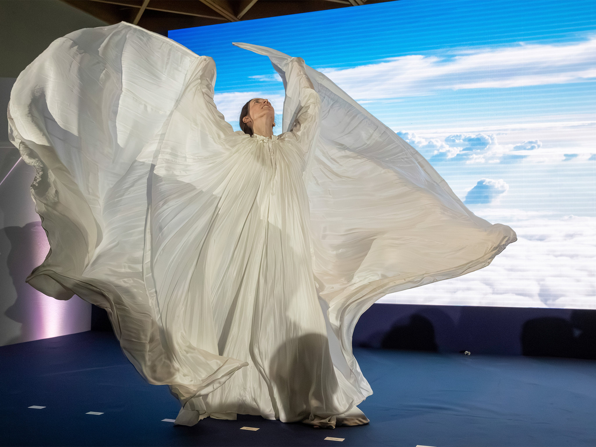 Performeuse en robe blanche ample devant un mur LED ROE VISUAL affichant un ciel nuageux
