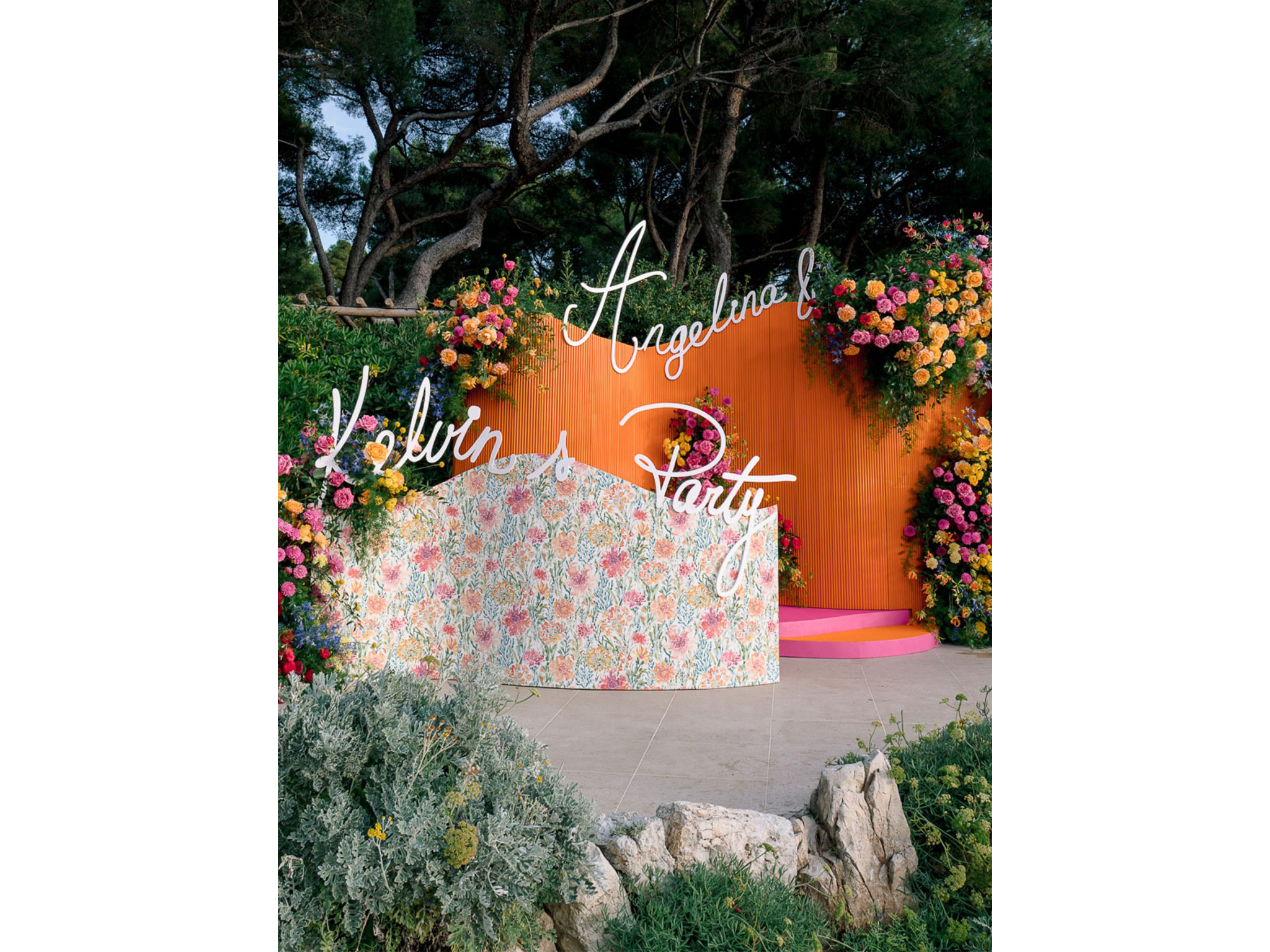 Panneau de bienvenue « Angelina & Kelvin's Party » en néon blanc sur fond orange corail, entouré de compositions florales colorées — décor fabriqué par AUCOP pour le Welcome Dinner à l'Hôtel du Cap Eden Roc, Antibes.