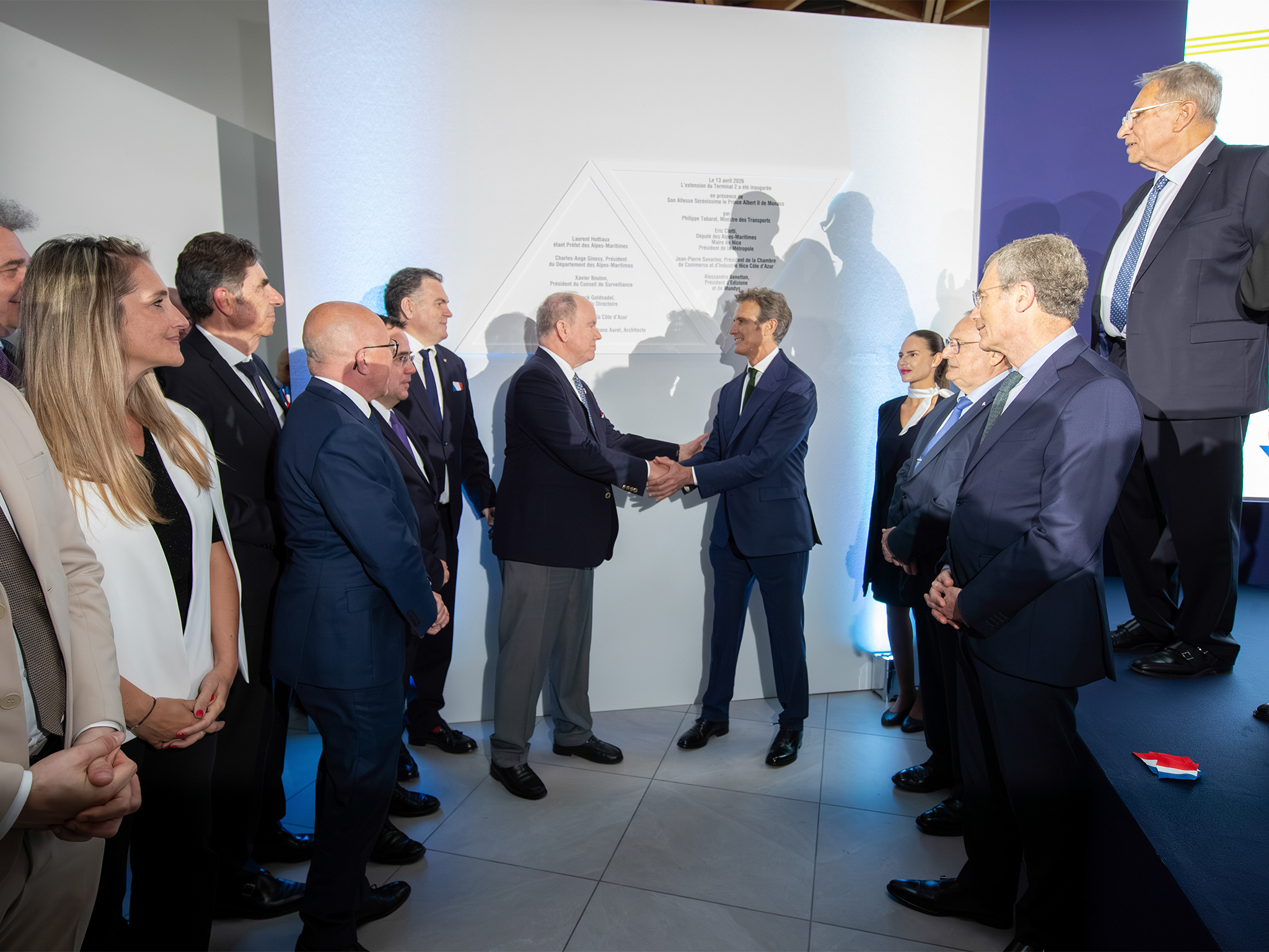 Poignée de main entre deux personnalités devant la plaque, entourées d'officiels lors de l'inauguration de l'extension de l'aéroport de nice