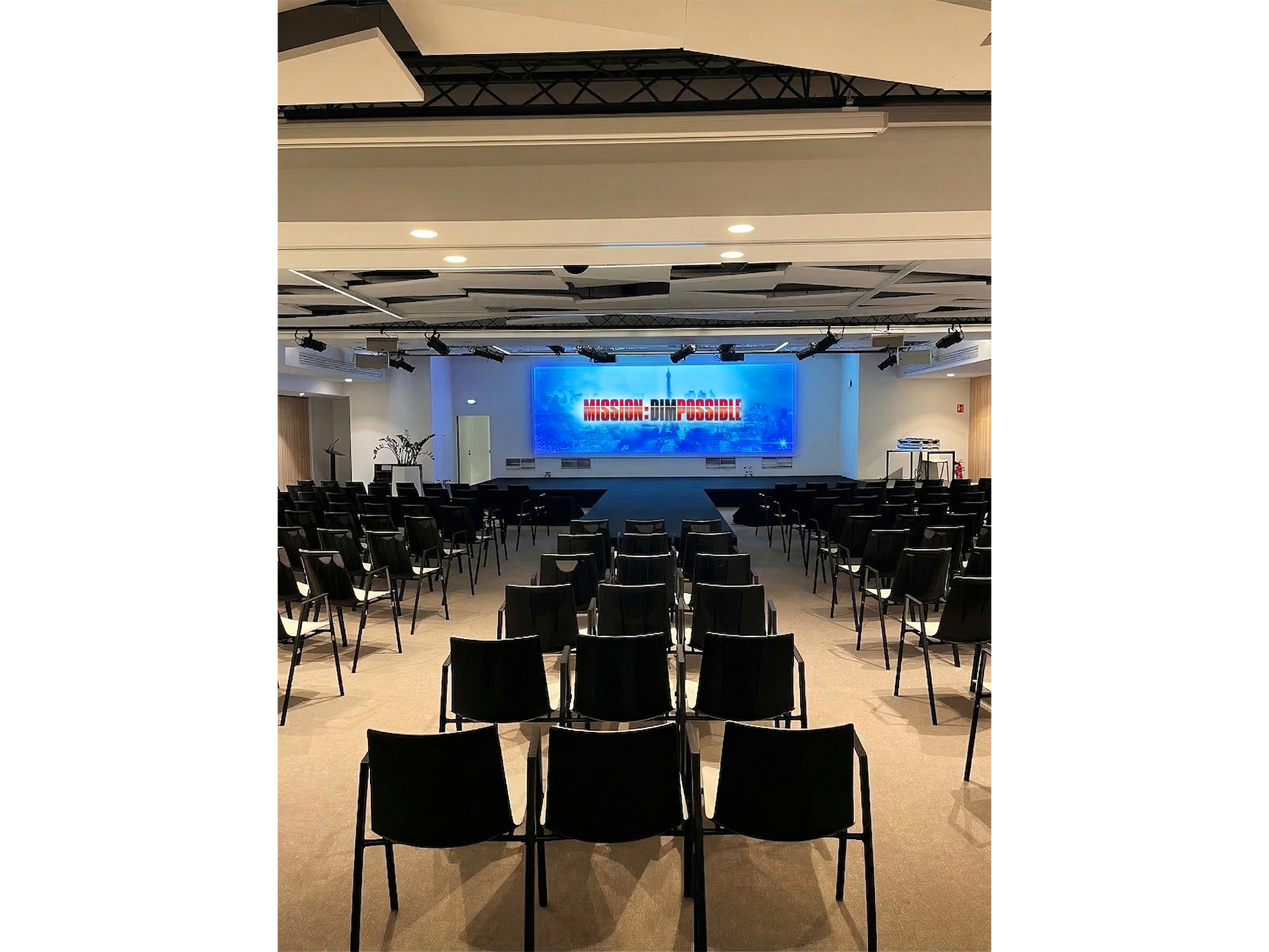 MISSION : DIMPOSSIBLE Salle de convention aménagée par AUCOP au World Trade Center Marseille Provence – allée centrale en moquette noire, chaises blanches et écrans de sol affichant le thème Mission DIMpossible