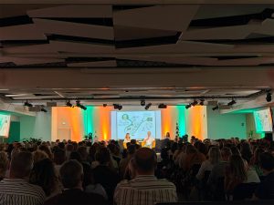 Plénière d'un séminaire d'entreprise au World Trade Center Marseille Provence : deux intervenants sur scène, grand écran de projection et éclairage vert et orange signés AUCOP, salle comble