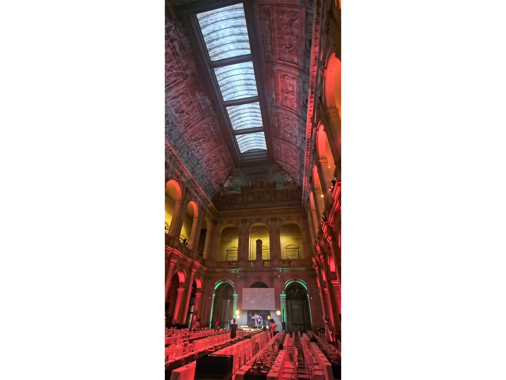Soirée de gala au Palais de la Bourse à Marseille : mise en lumière architecturale rouge et verte et dîner dressé sous la verrière, dispositif AUCOP