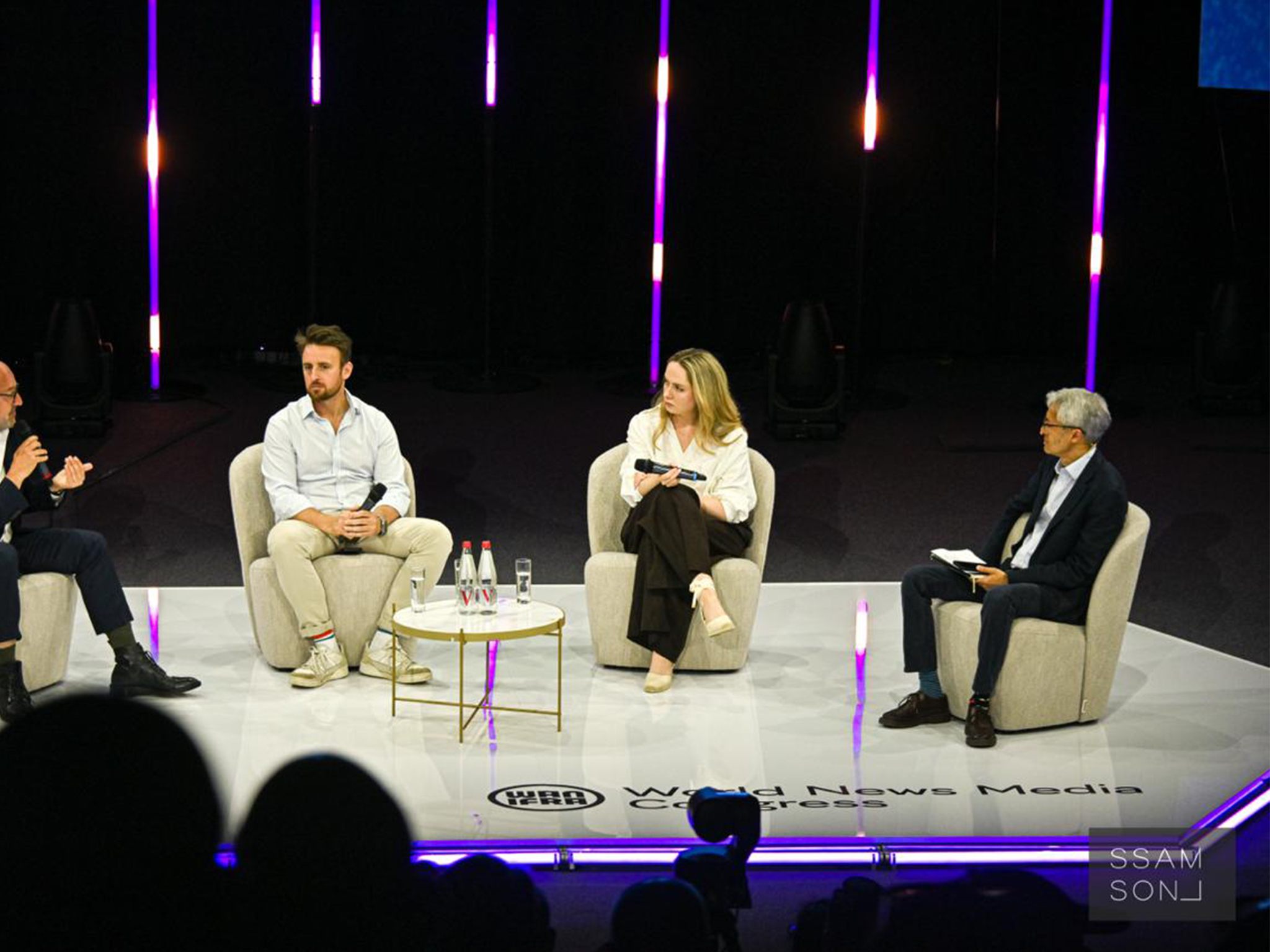 Panel de quatre intervenants en fauteuils sur la scène hexagonale, micros HF Shure et DPA déployés par AUCOP pour le World News Media Congress.