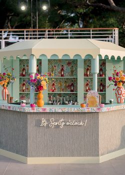 Bar à spritz octogonal sur mesure conçu et fabriqué par les ateliers AUCOP pour le Welcome Dinner d'Angelina & Kelvin à l'Hôtel du Cap Eden Roc — structure vert menthe, toit crème à festons, habillage fleuri et enseigne néon « It's Spritz o'clock ! », Antibes.